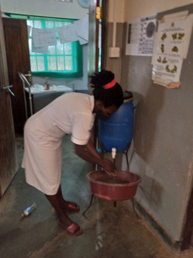 A Nurse at Ongako Health Centre using handwashing facility provided by RHITES-N Acholi project. Above her is are posters to remind health workers on handwashing