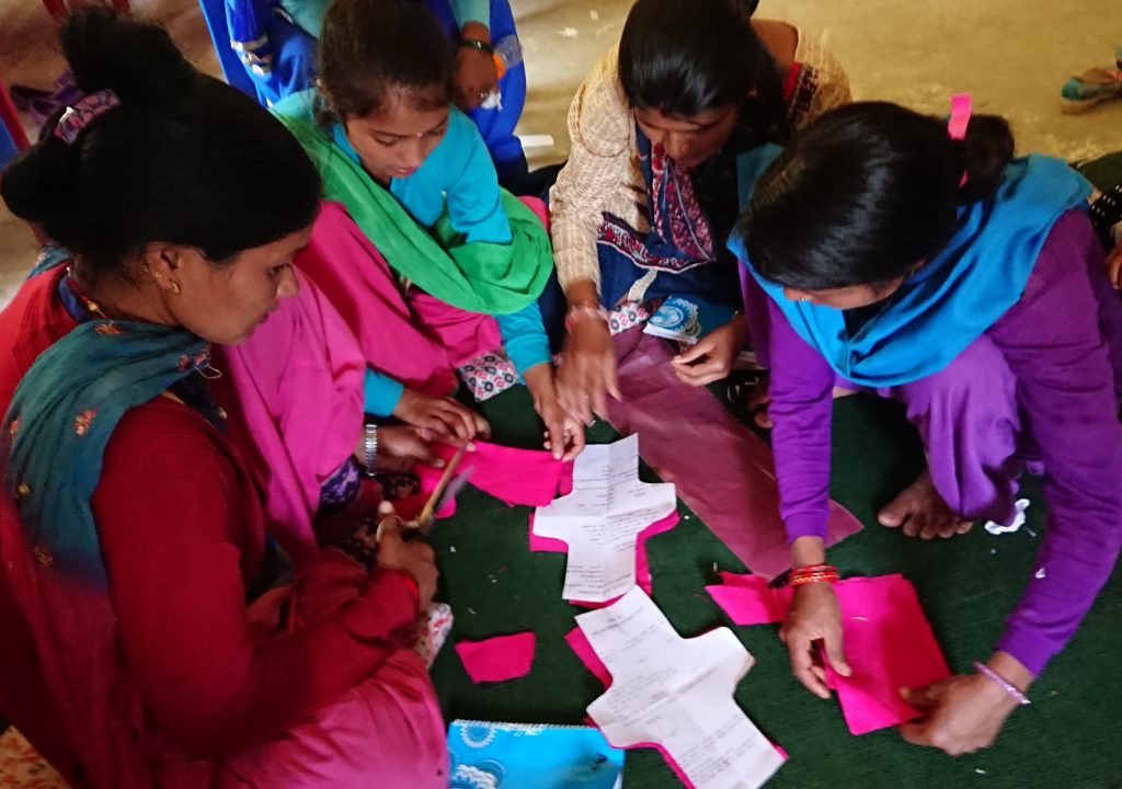 Group of 4 women sitting together in a group making reusable sanitary pads. Set in rural mountanious village in rural Nepal