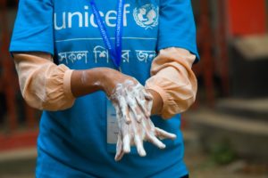 Person wearing a blue UNICEF t-shirt. Mid-shot just showing person's torso, arms and hands. They are rubbing soapy hands together. The t-shirt also has Hindi writing on it.