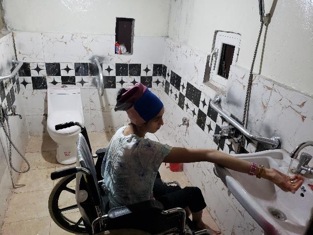 A young woman in a wheelchair washes her hands in a bathroom equipped with mobility aids