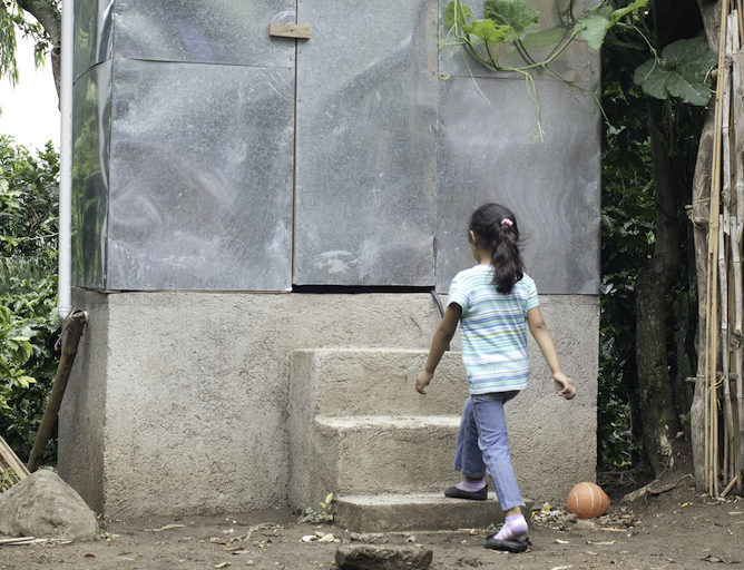A Nicaraguan community-based organization’s composting latrine. Young girl walking towards latrine about to go up some steps.